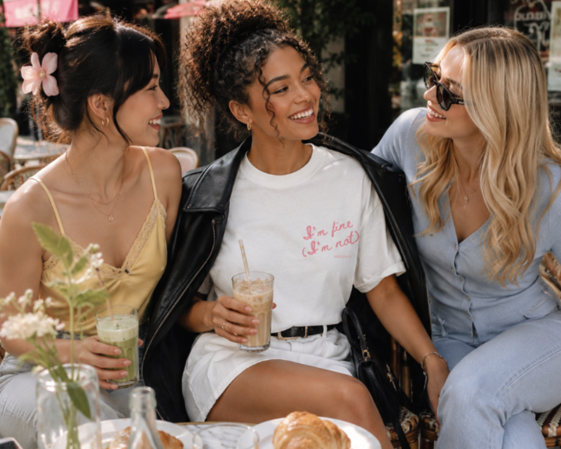 Three women sitting at an outdoor cafe table, enjoying drinks and food.