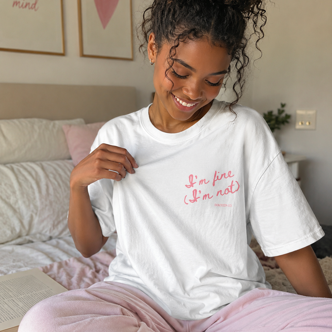 Woman wearing a white t-shirt with text, sitting on a bed in a bedroom.